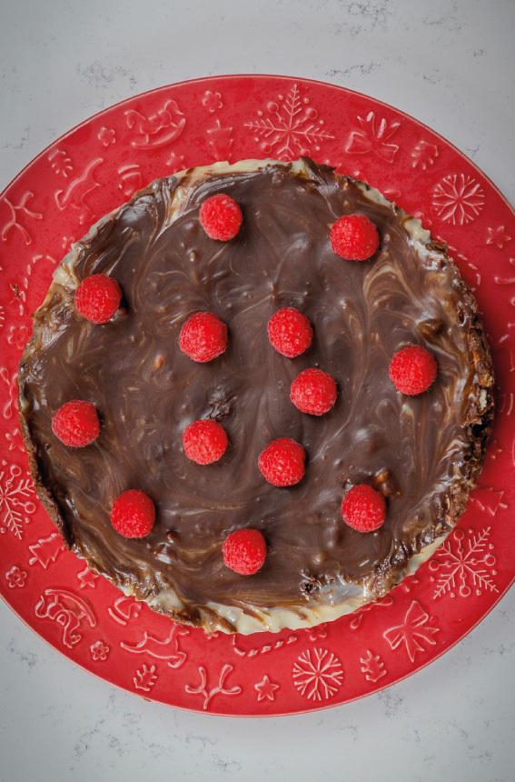 prato vermelho, com um bolo redondo, com cobertura de chocolate derretido, enfeitado com framboesas frescas.