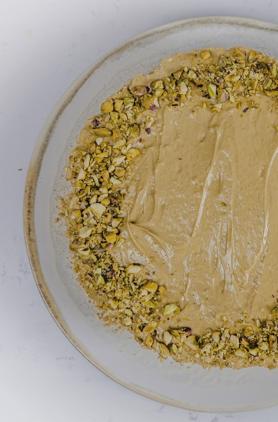Vista de cima do Bolo redondo com creme aveludado de pistacho, em cima polvilhado com pistachio triturado a toda a volta do bolo.